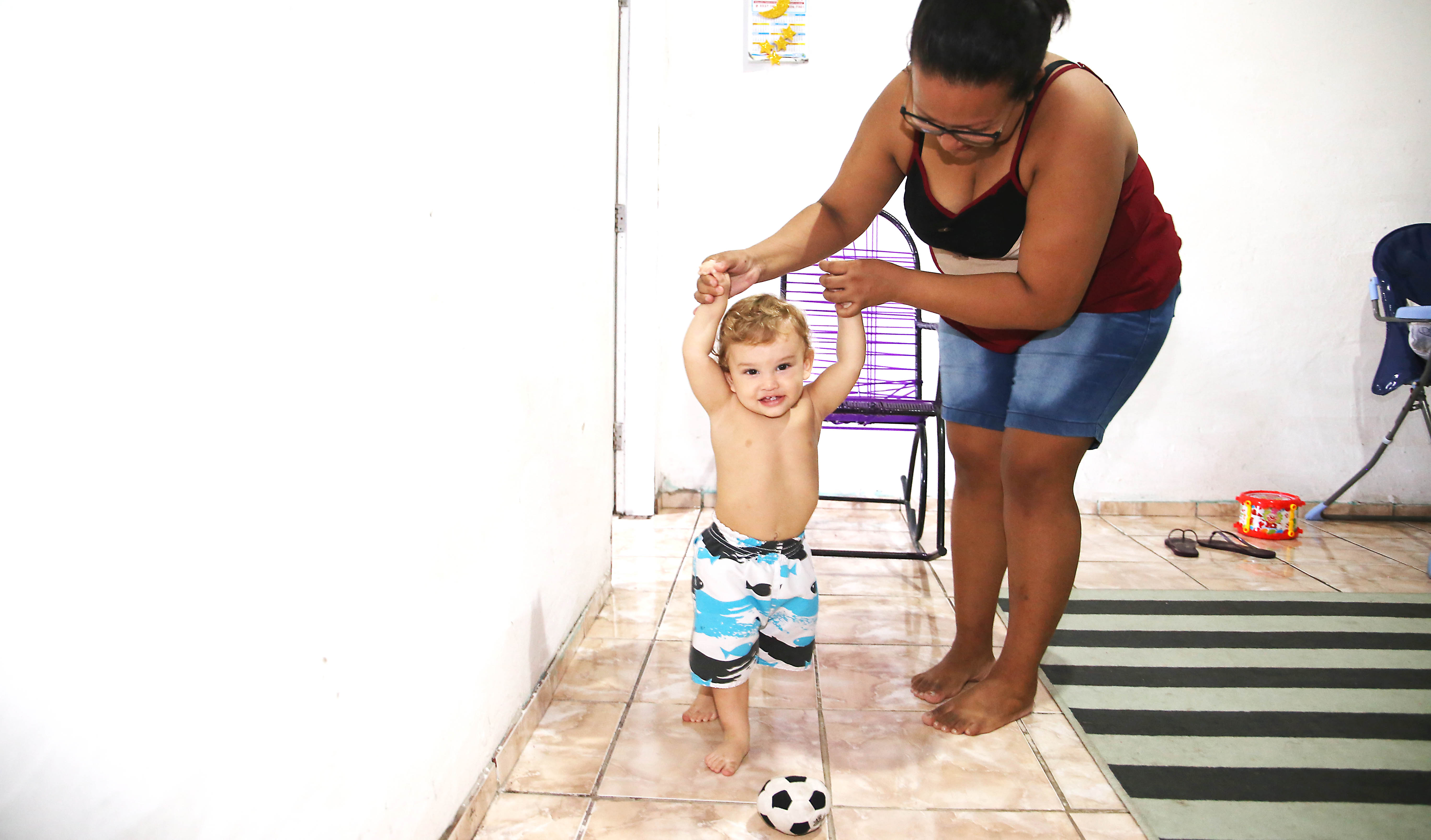 mãe segurando braços de filho bebê andando atrás de bola